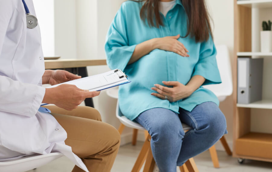 pregnant woman sitting at the desk in doctor's office visiting clinic. Health provider holding report file and giving consultation during medical exam