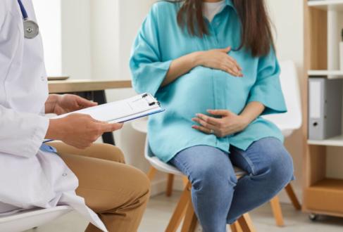 pregnant woman sitting at the desk in doctor's office visiting clinic. Health provider holding report file and giving consultation during medical exam