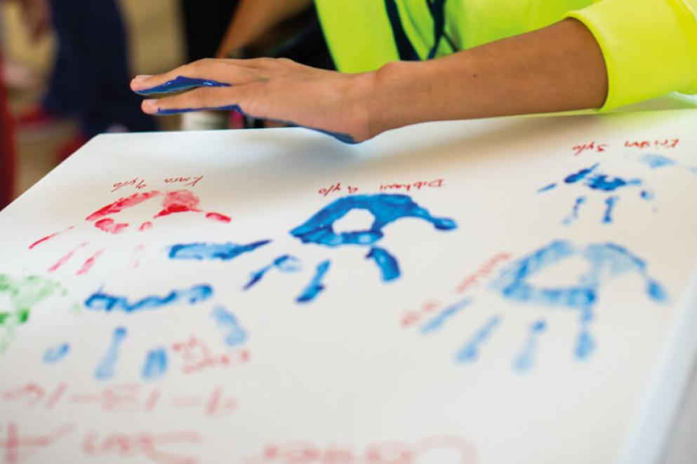 A child prepares to press their painted alongside other handprints.